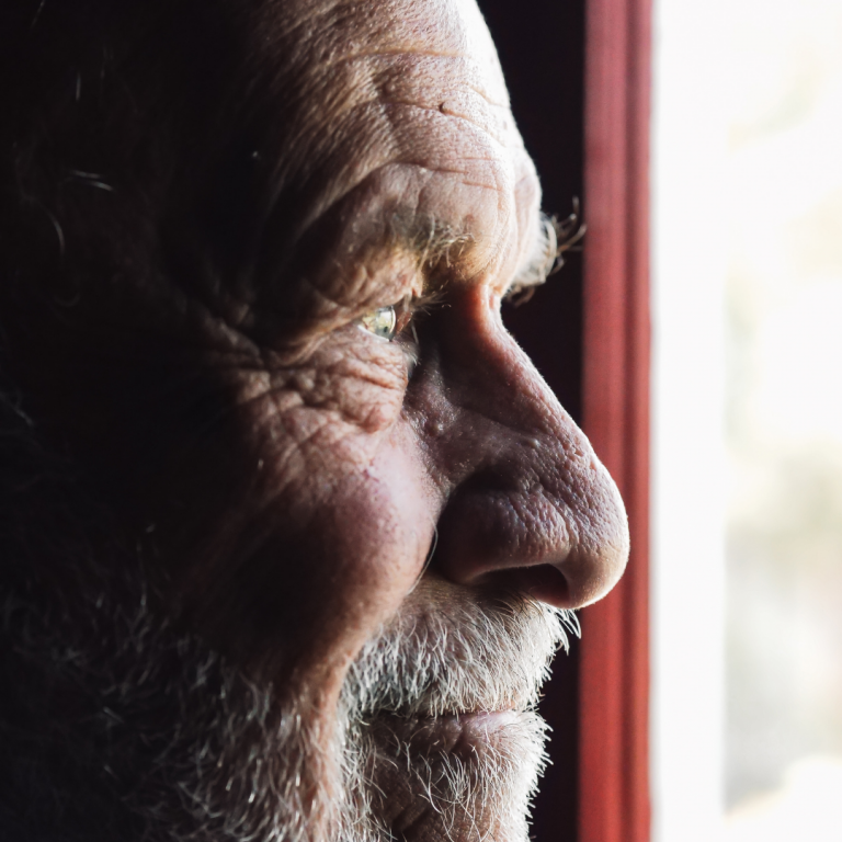 An elderly man looking out a window